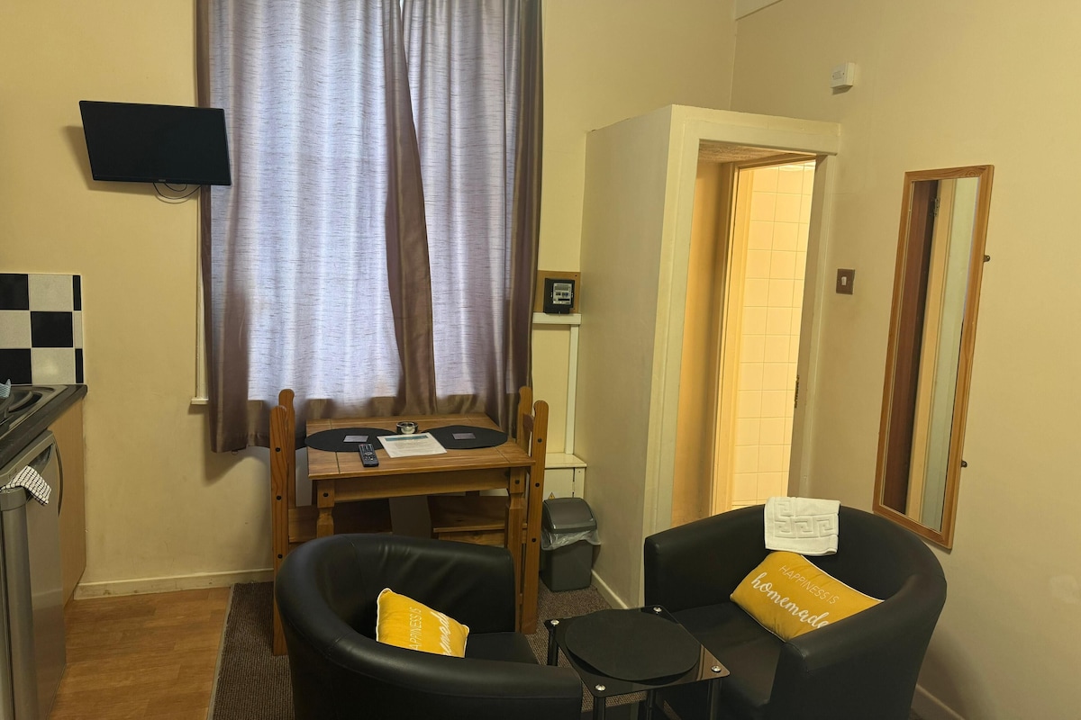 A small, well-lit room with a desk, two chairs, a television, and a door leading to another room.