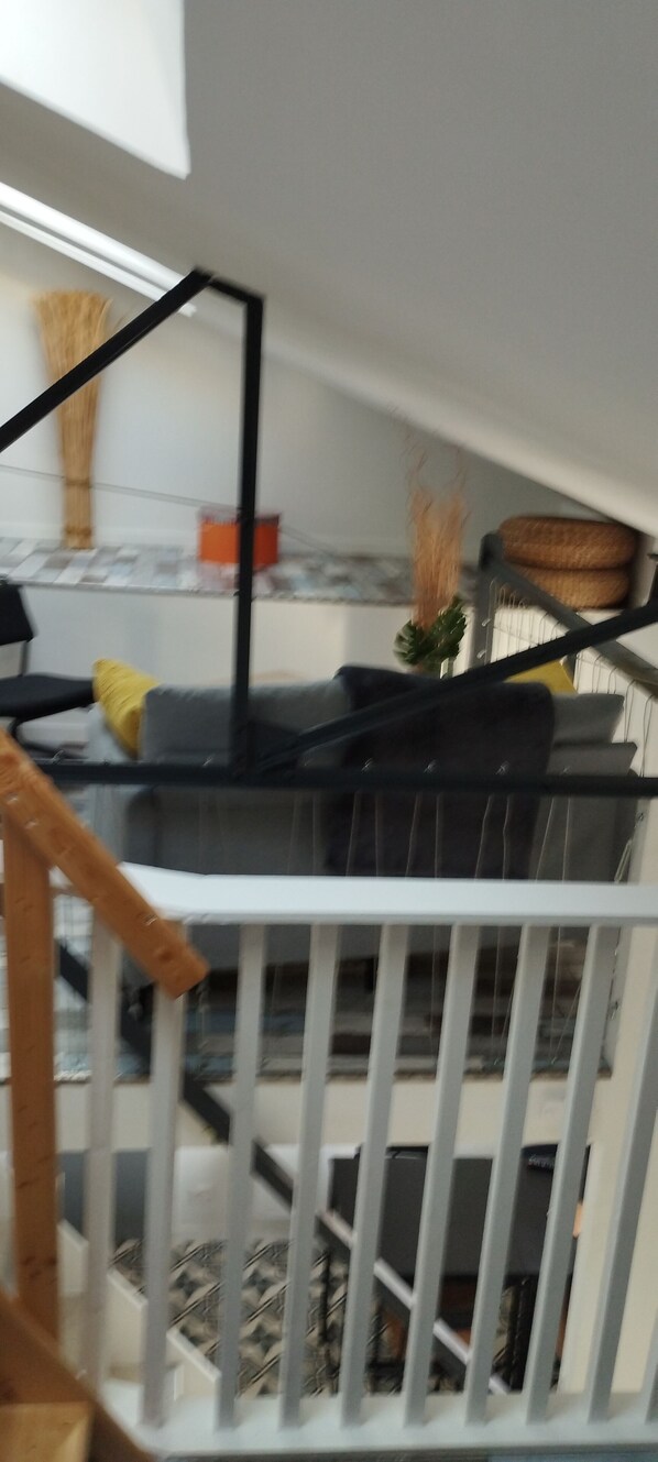 A room with a white railing, a black sofa, and a small table with a vase. - Duplex apartment Loft (DAINVILLE)
