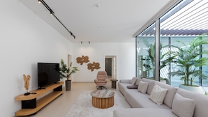 Una sala de estar moderna con un televisor de pantalla plana grande, un sofá color beige, una mesa de centro redonda de madera y una planta en maceta.