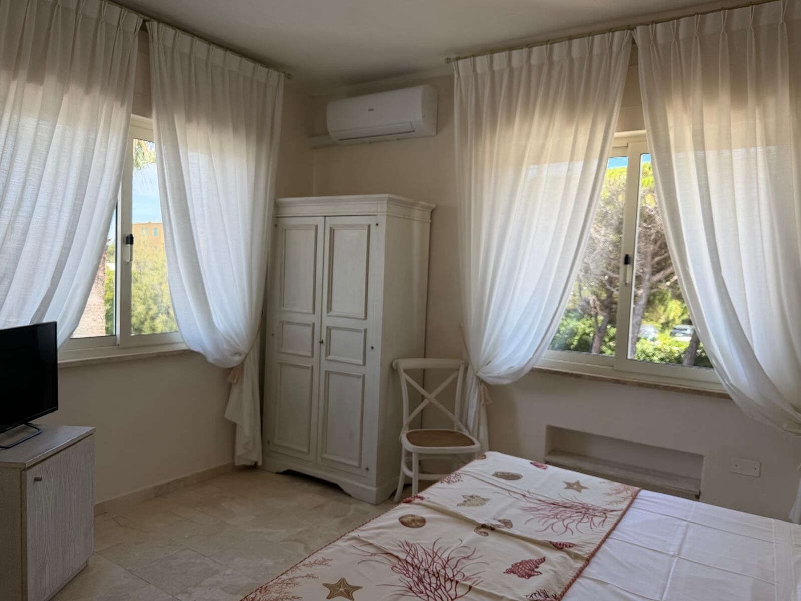 A bedroom with a bed, a TV on a cabinet, a wardrobe, and a chair.