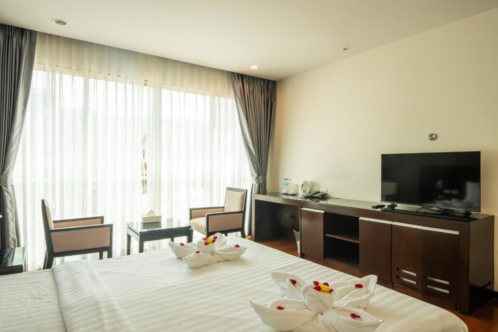 A hotel room with a bed, a desk, a TV, and a window with curtains.