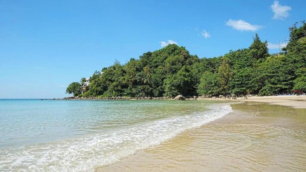 A beach with clear turquoise water, a sandy shore, and dense green foliage on a hillside. - Yenna Apartment (Kamala)