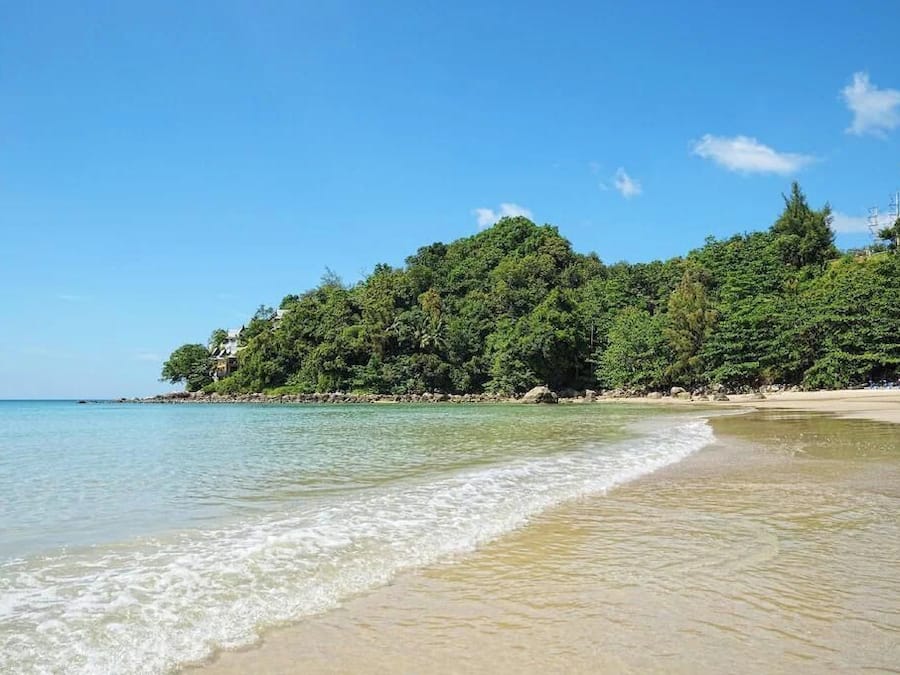 Una playa con agua turquesa cristalina, una orilla arenosa y densa vegetación verde en una colina.