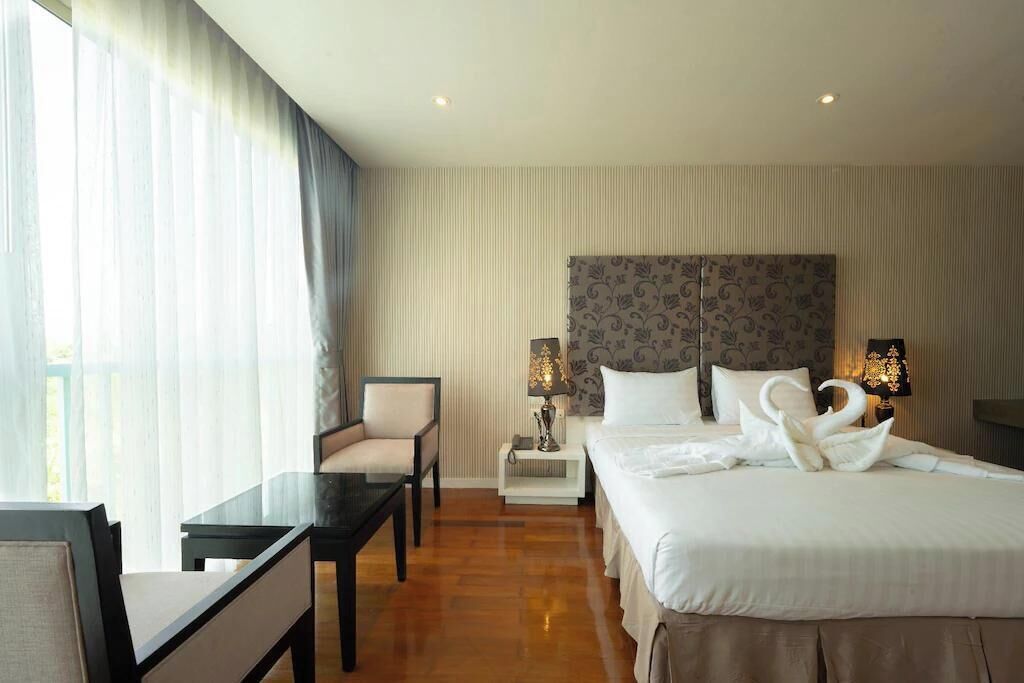 A hotel room with a bed, a desk, a chair, a nightstand with lamps, and a window with curtains.
