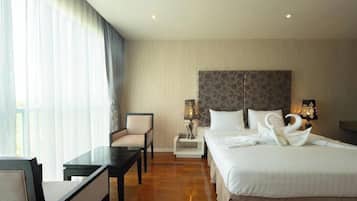A hotel room with a bed, a desk, a chair, a nightstand with lamps, and a window with curtains.