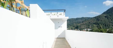 A narrow, white-walled corridor leading to a balcony with a view of a mountainous landscape.