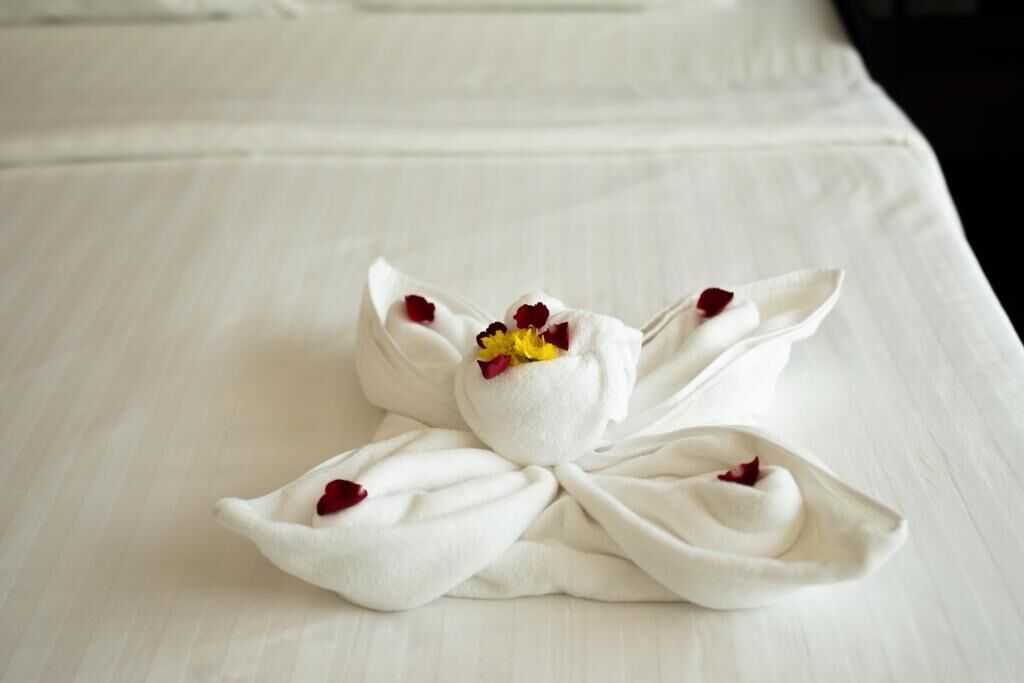 A neatly folded towel with a flower arrangement on a bed.
