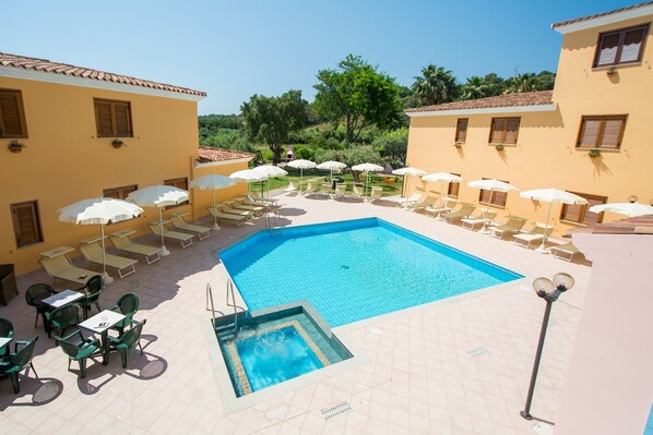 A pool area with sun loungers and umbrellas, surrounded by buildings with tiled roofs and windows. - Spacious Apartment With Shared Pool (Orosei)