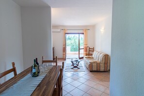 Un coin repas avec une table en bois dressée pour deux personnes, un canapé et une vue sur l’extérieur.