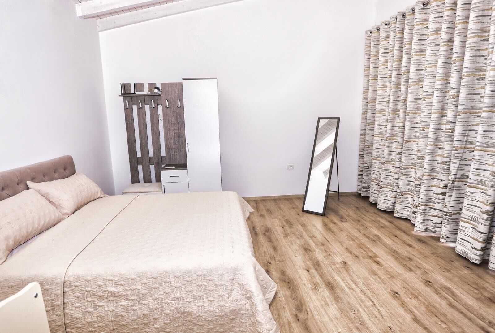 A bedroom with a bed, a wardrobe, a mirror, and a curtain.