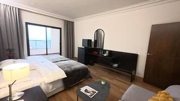 Una habitación de hotel moderna con una cama, un escritorio con lámpara, una mesita con una revista, un sofá, un banco y un armario.