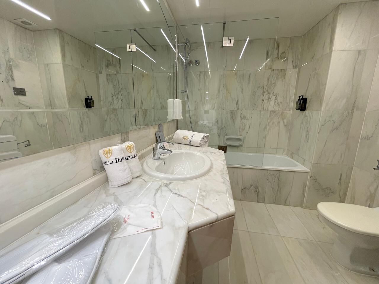 Un bany modern amb parets de marbre, un lavabo gran, una banyera i un vàter.