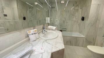 Un bany modern amb parets de marbre, un lavabo gran, una banyera i un vàter.