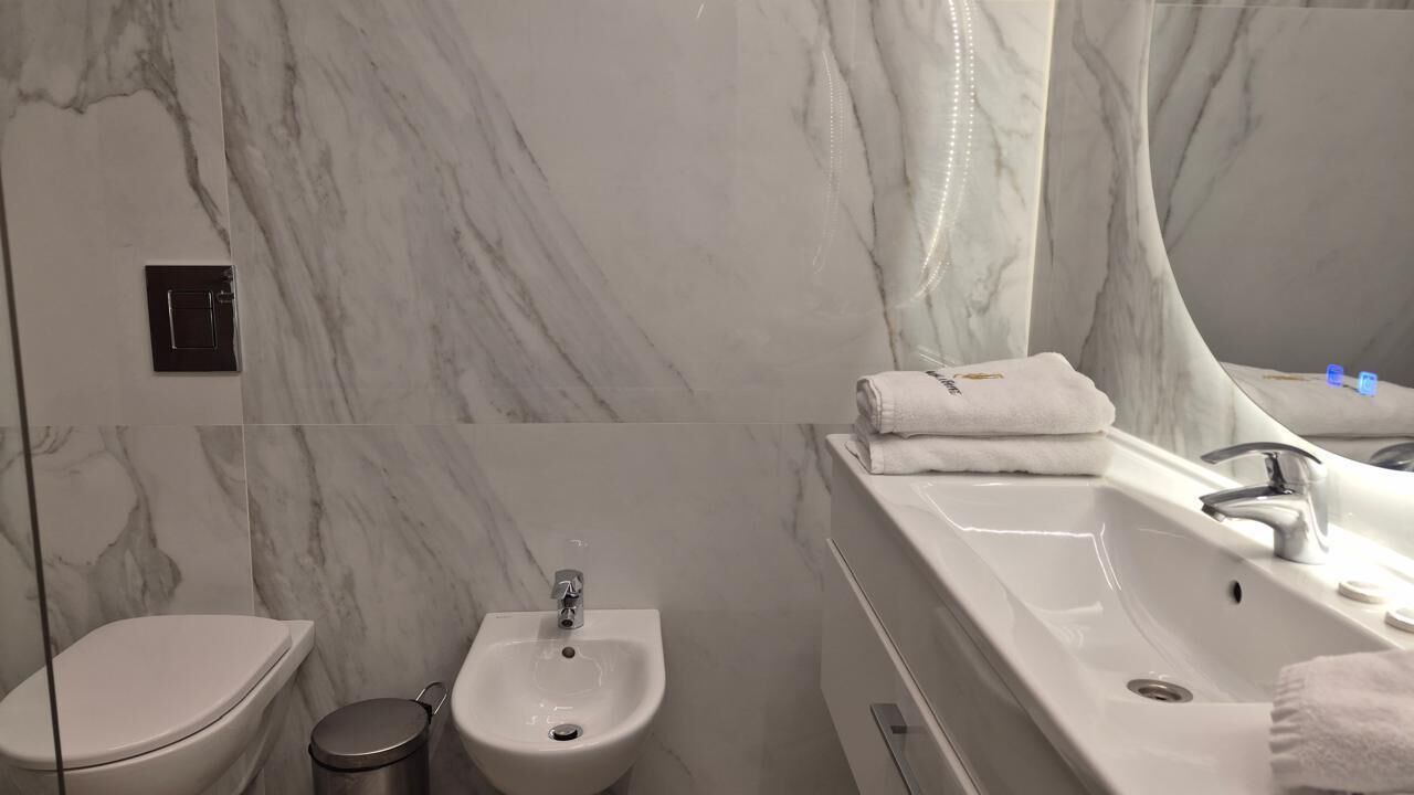 A modern bathroom with a marble wall, a bidet, a sink with a mirror, and a towel on the counter.