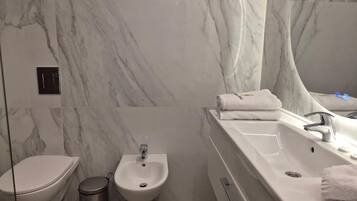 A modern bathroom with a marble wall, a bidet, a sink with a mirror, and a towel on the counter.