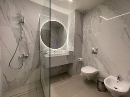 Moderni kylpyhuone, jossa on lasiseinällä varustettu suihku, pyöreä peili, pesuallas ja wc.