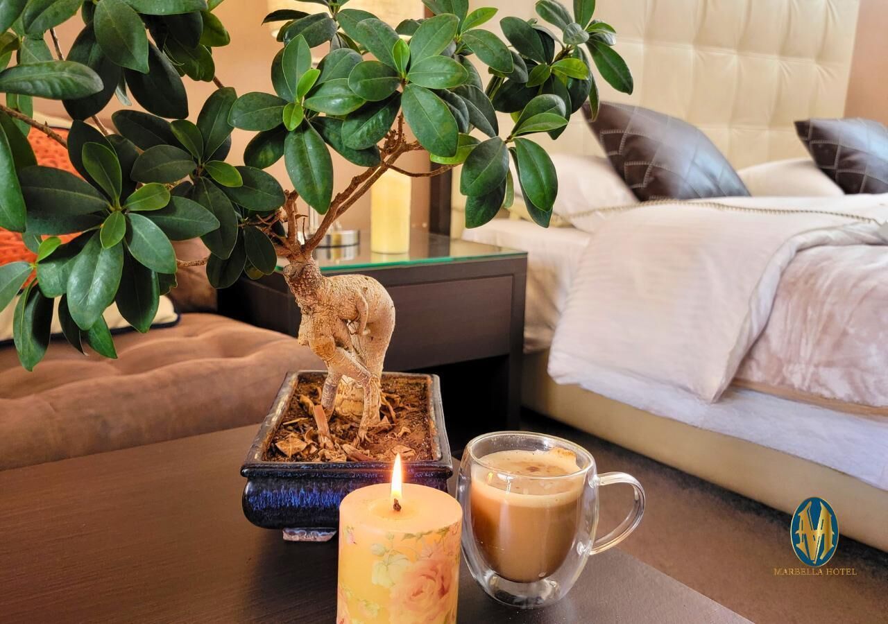 A bedroom with a bed, a nightstand, a potted plant, a candle, and a glass mug.