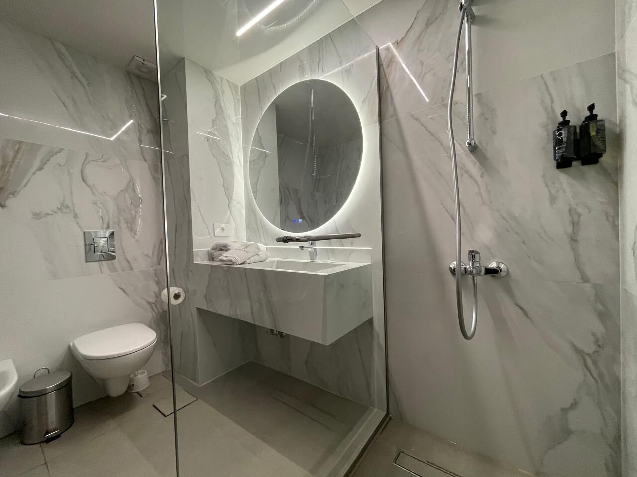 A modern bathroom with a glass-enclosed shower, a round mirror, and a white sink.