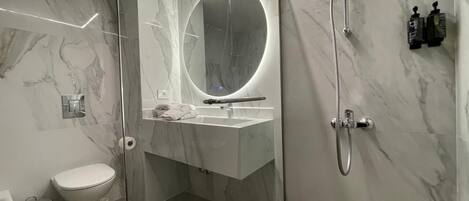 A modern bathroom with a glass-enclosed shower, a round mirror, and a white sink.