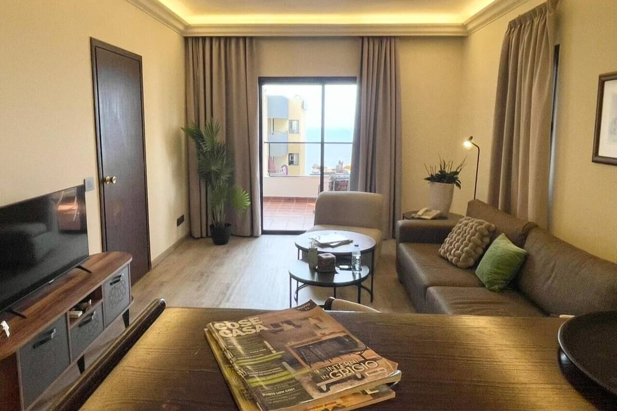 A hotel room with a flat-screen TV, a sofa, a coffee table, and a balcony with a view.