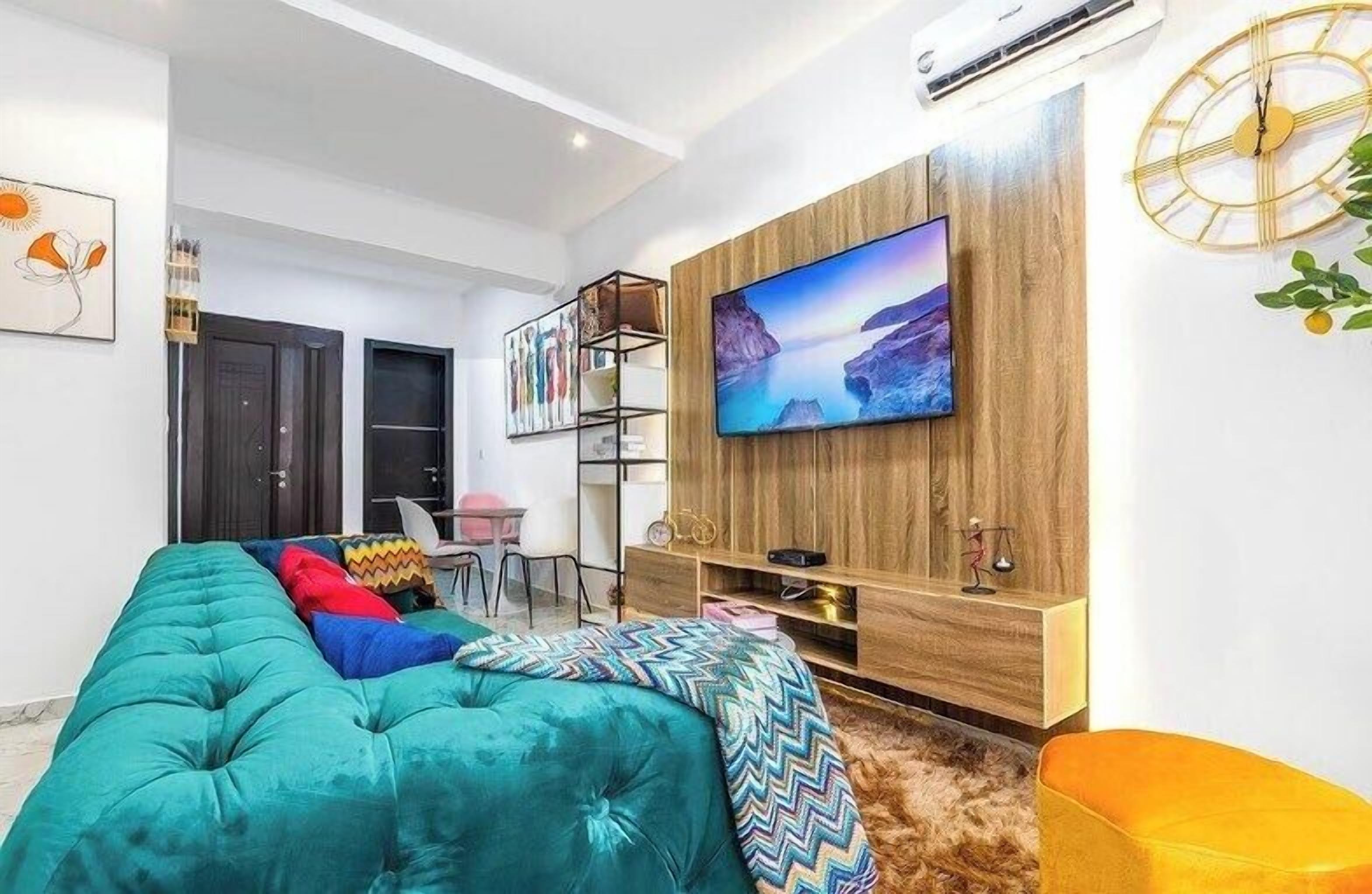 Un salon moderne avec un grand téléviseur à écran plat fixé à un mur en bois, un canapé turquoise et un petit fauteuil orange.