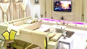 A modern living room with a beige sofa, a glass coffee table, and a flat-screen TV mounted on the wall. - Favour Shortlet Apartment (Lagos)