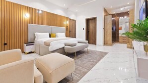 A modern bedroom with a large bed, bedside tables, a seating area, and a wooden accent wall. - Favour Shortlet Apartment (Lagos)