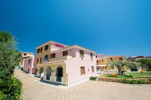 A pink villa with a tiled roof, a pool, and a garden with orange chairs. - Comfy Flat With Terrace and Pool (Orosei)