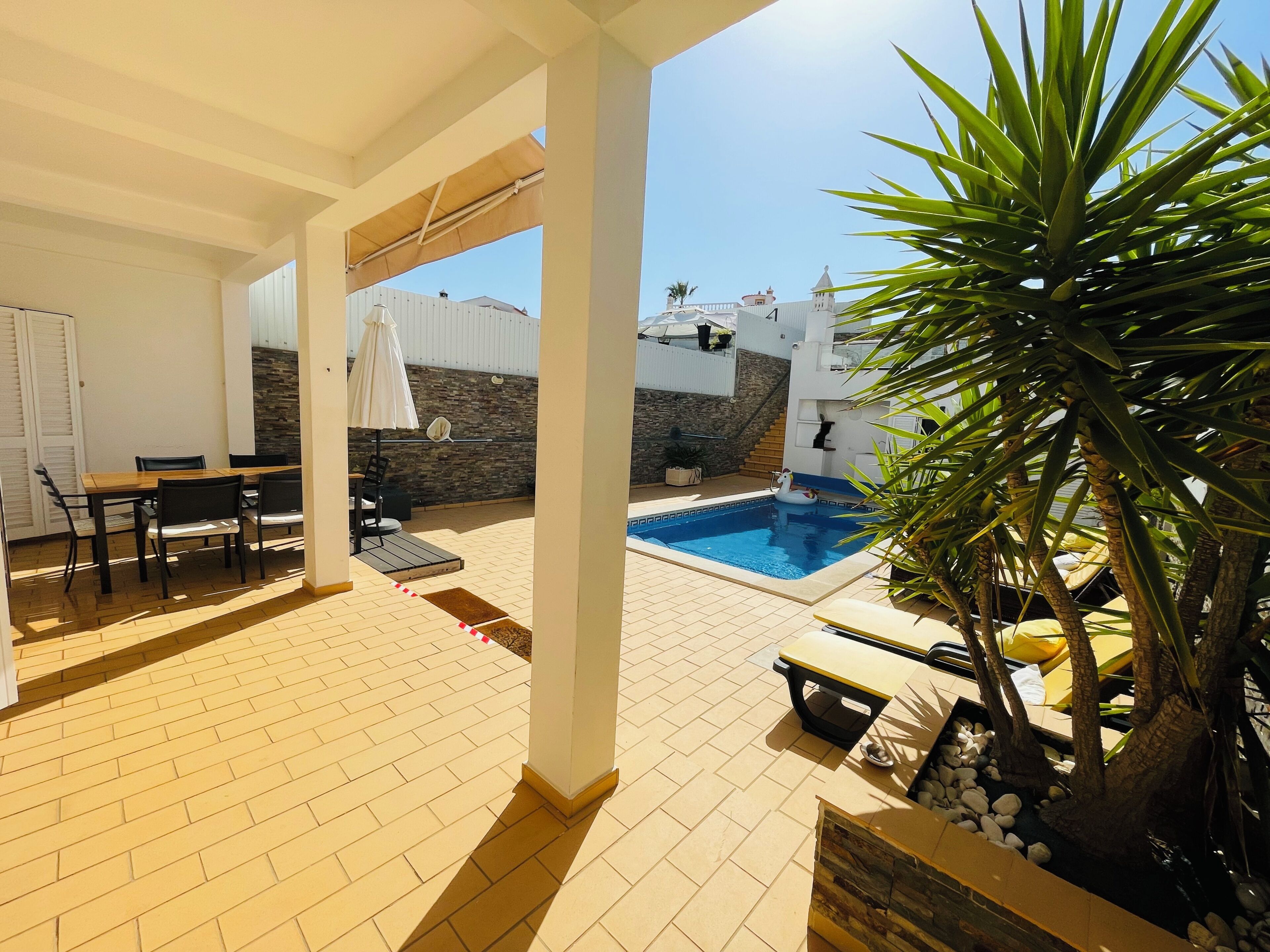 A covered outdoor area with a pool, a dining table, and chairs.
