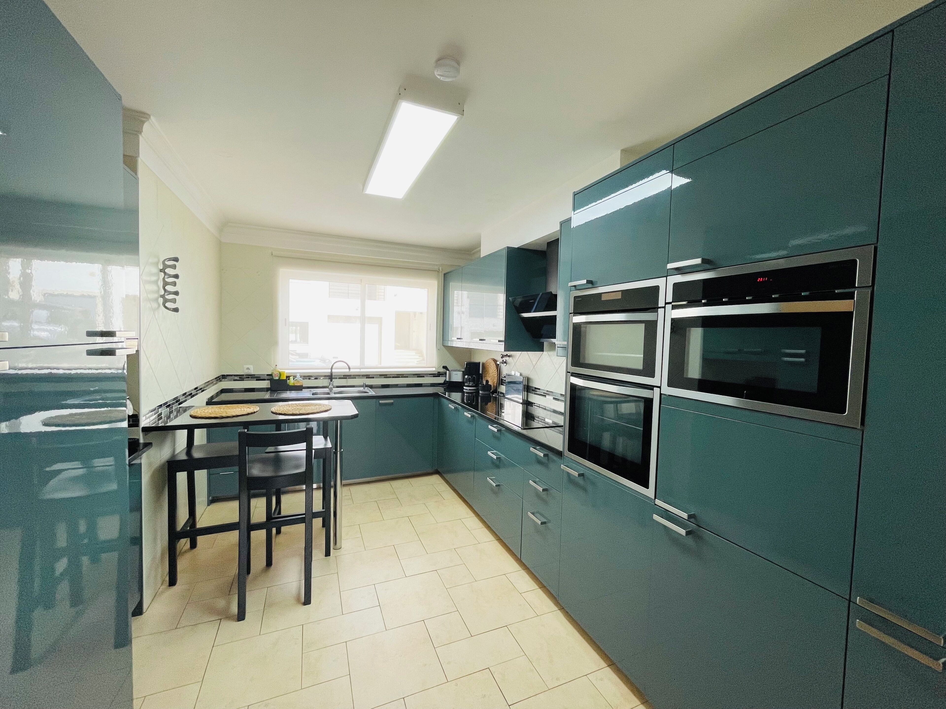 A kitchen with teal cabinets, a double oven, and a window providing natural light.