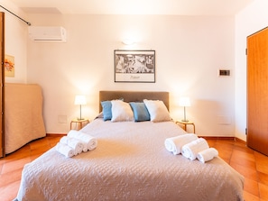 Un letto rifatto con copriletto trapuntato, due lampade da comodino e un quadro appeso al muro.