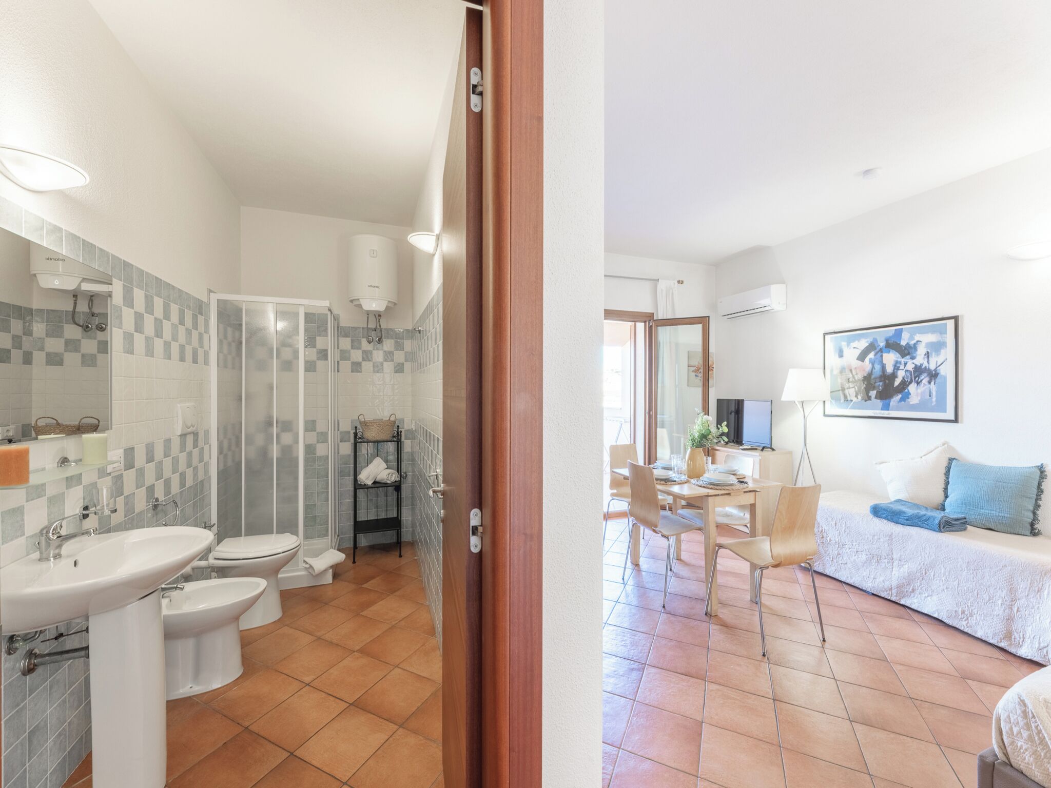 Une salle de bain moderne avec douche, toilettes et lavabo. On y trouve également un coin repas avec une table et des chaises, ainsi qu’un salon avec un canapé et un tableau au mur.
