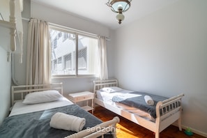 A room with two single beds, a small bedside table, a window with curtains, and a ceiling light fixture. - 2 Bedroom Apartment in Downtown Floripa Ebe0804 (Florianópolis)