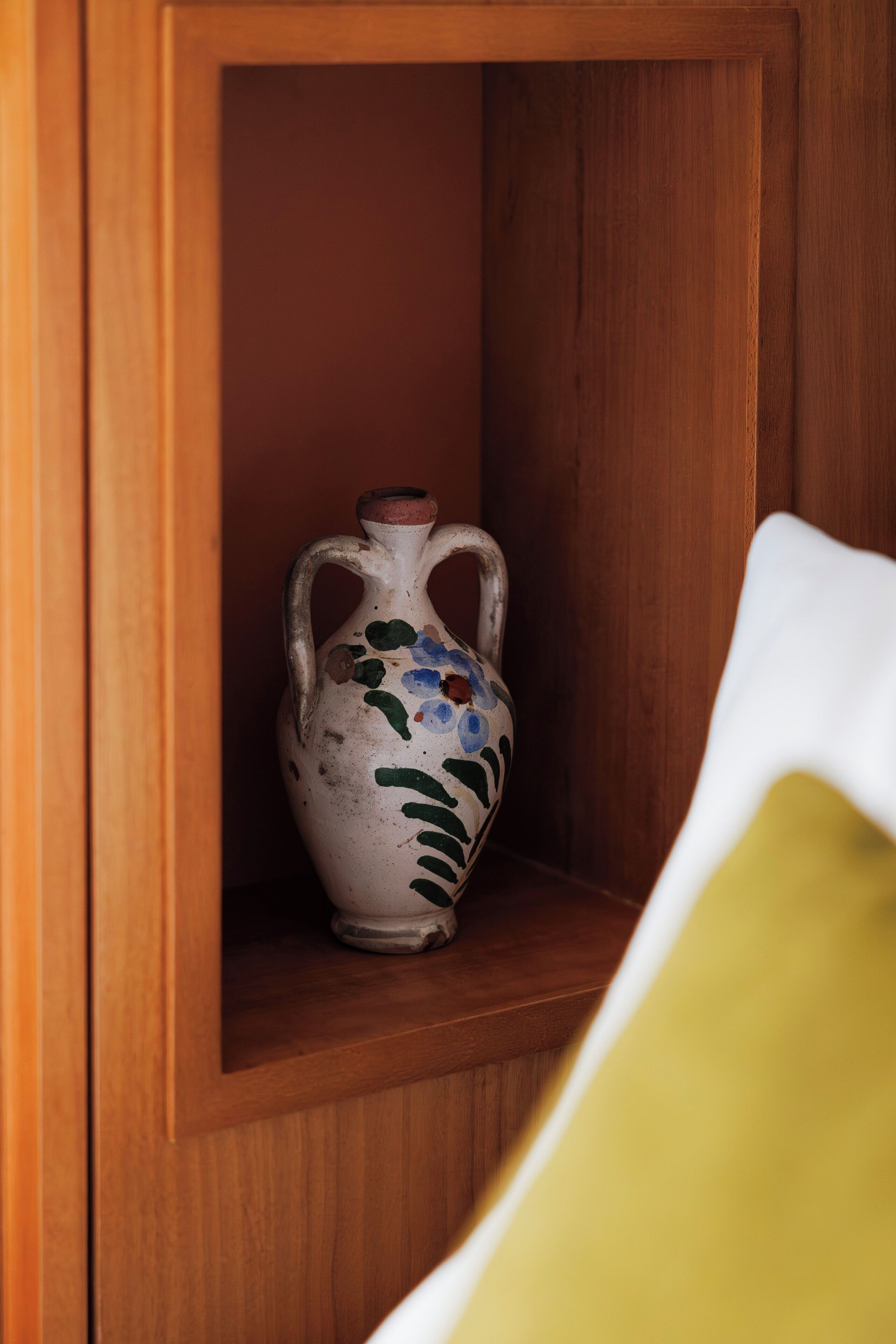 A wooden cabinet with a white vase featuring floral patterns.