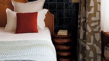 A neatly made bed with white and red pillows, a wooden headboard, and a small bedside table with a book.