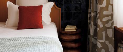 Una cama bien hecha con almohadas blancas y rojas, un cabecero de madera y una mesita de noche con un libro.