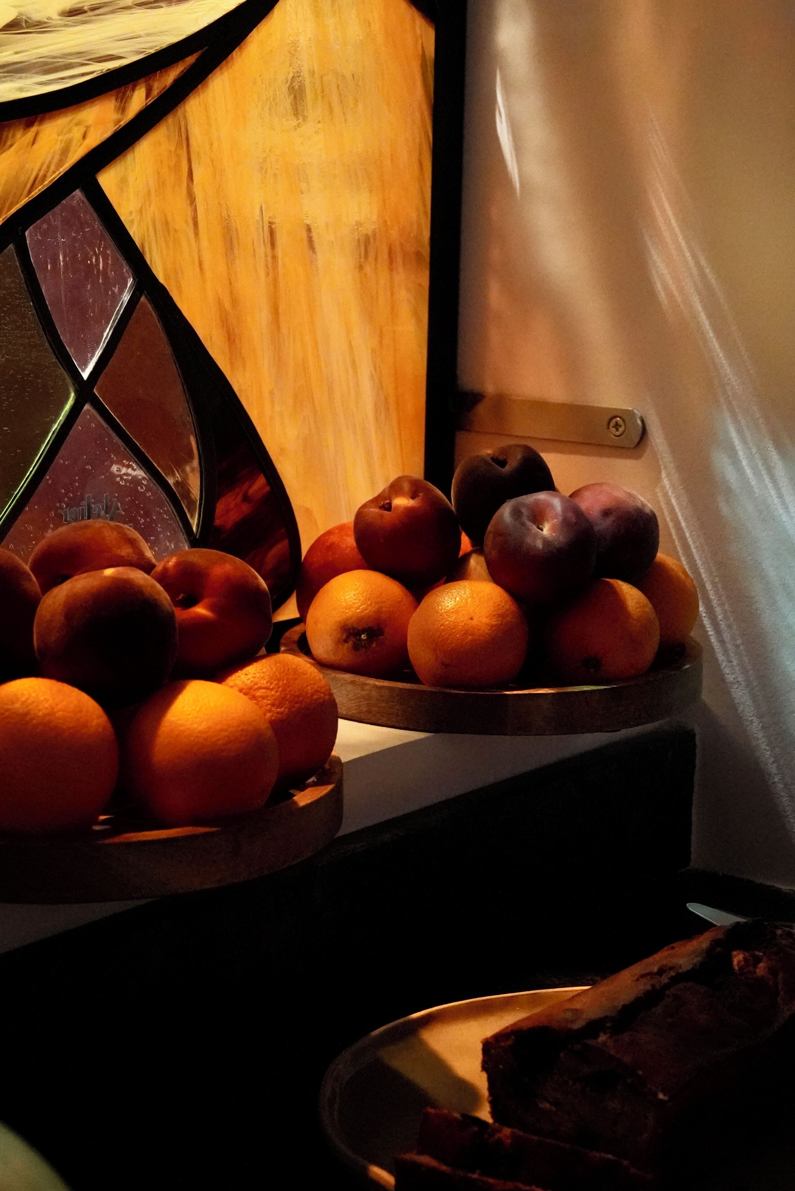 A wooden table with a fruit bowl containing oranges and plums.