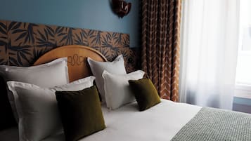 A neatly made bed with white and olive green pillows, a patterned headboard, and a window with sheer curtains.