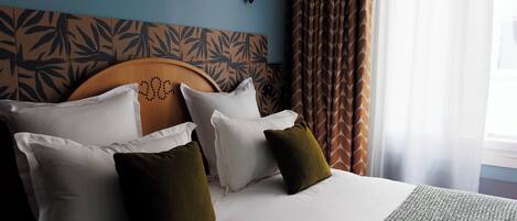 A neatly made bed with white and olive green pillows, a patterned headboard, and a window with sheer curtains.