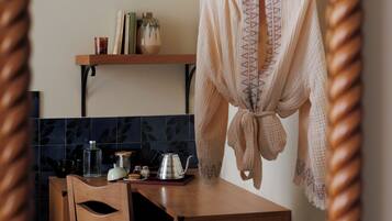 A kitchen with a wooden table, a chair, a hanging garment, and a shelf with kitchen items.
