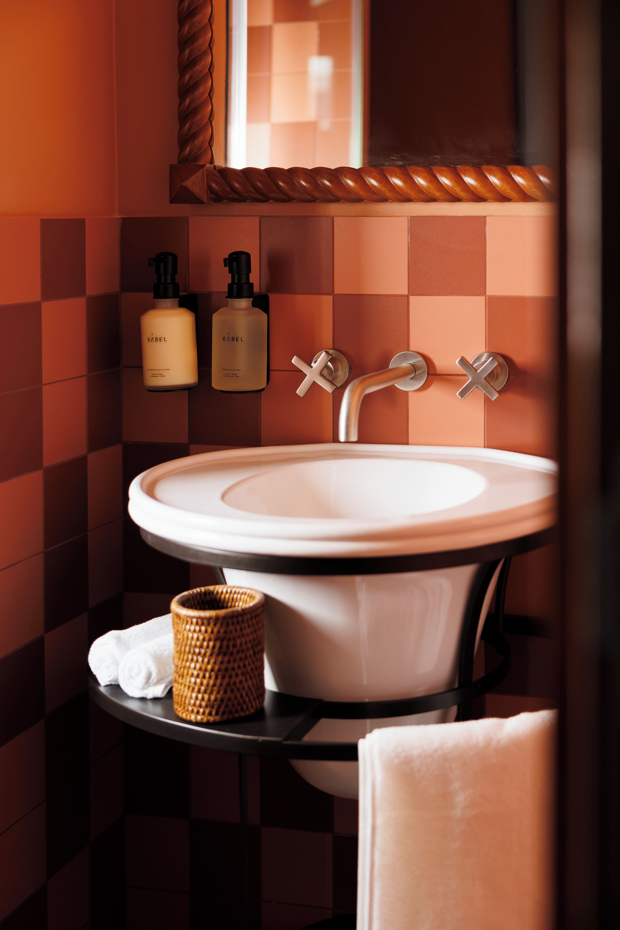 A bathroom with a white sink, two soap dispensers, a towel, and a woven basket.