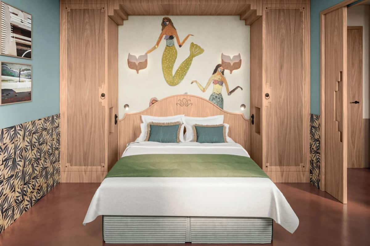 Un dormitorio con un gran mural de sirenas en la pared, un cabecero de madera y una cama con colcha verde.