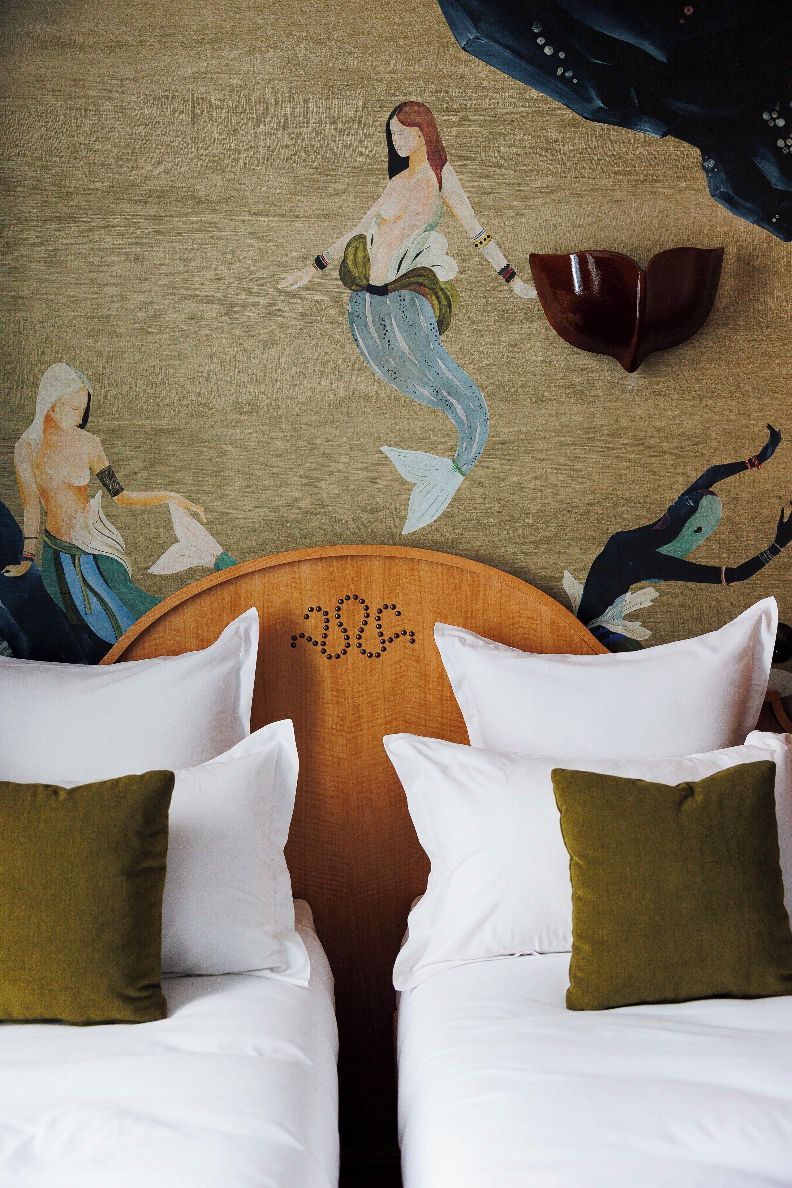 A room with two beds, a wooden headboard, and a mural of mermaids on the wall.