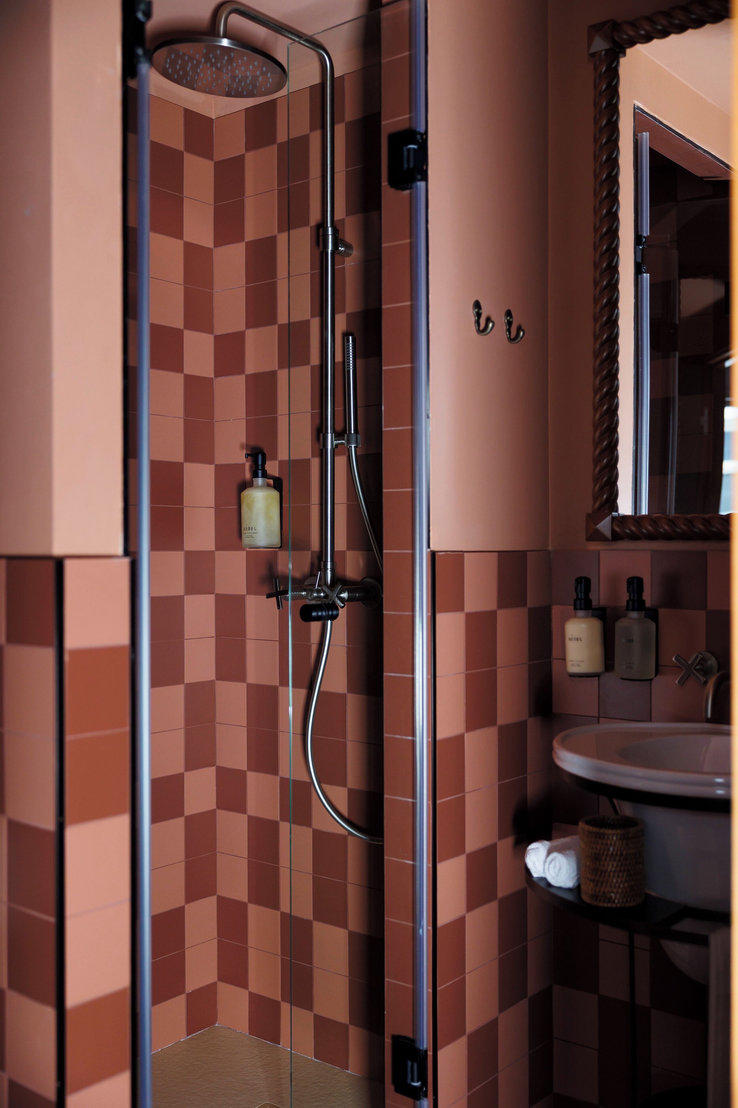 A bathroom with a checkered tile wall, a shower, a sink, and two bottles of shampoo.