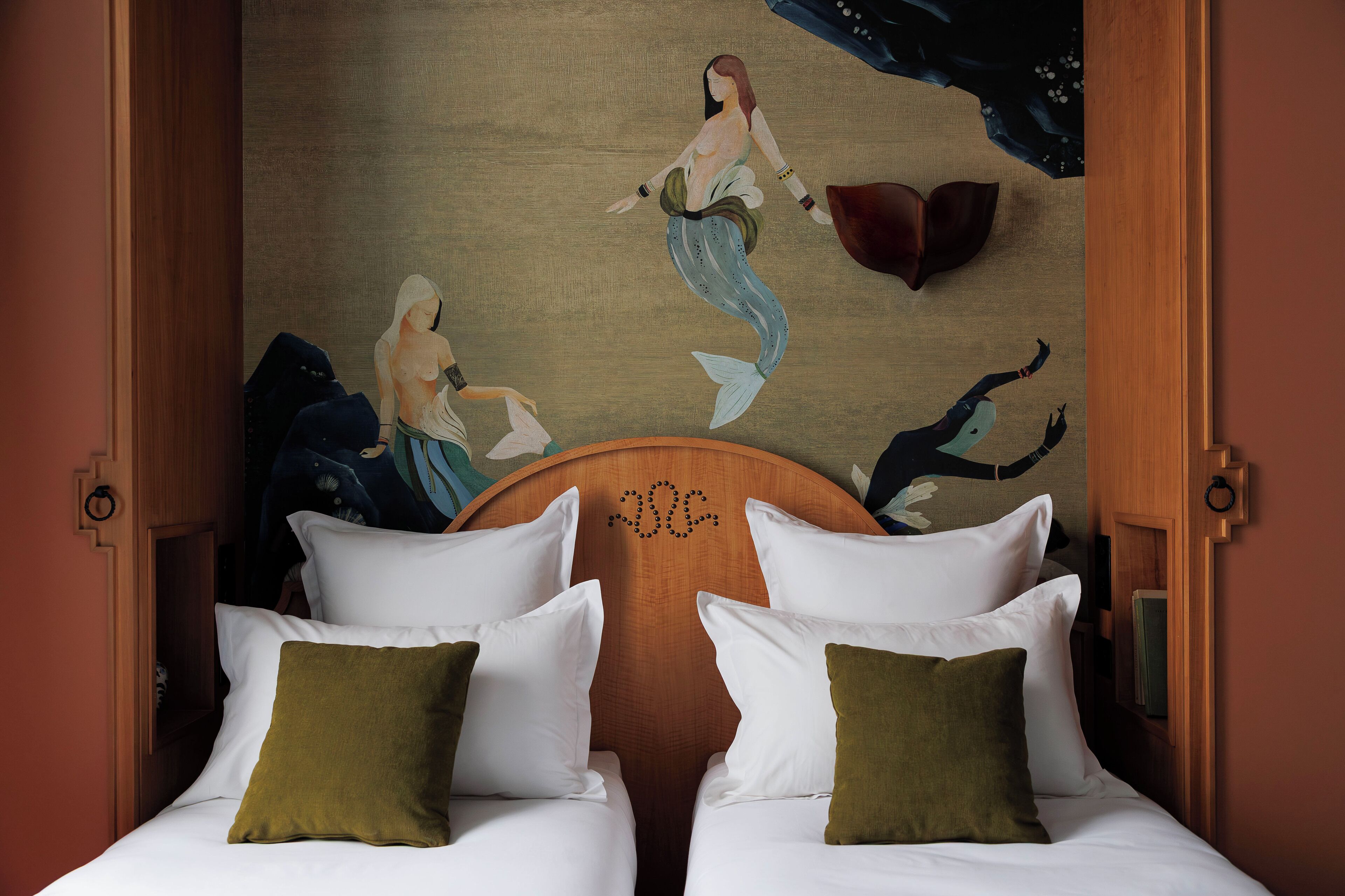 A hotel room with two beds, a mural of mermaids on the wall, and a wooden headboard.