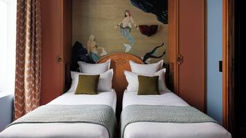 A hotel room with two beds, a mural on the wall, and a window with curtains.