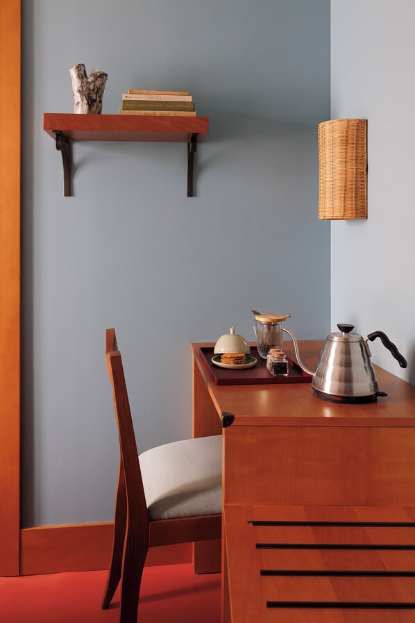 Ein Holztisch mit einem Stuhl, ein Regal mit Büchern und einer Vase, eine Lampe und eine Kaffeemaschine.