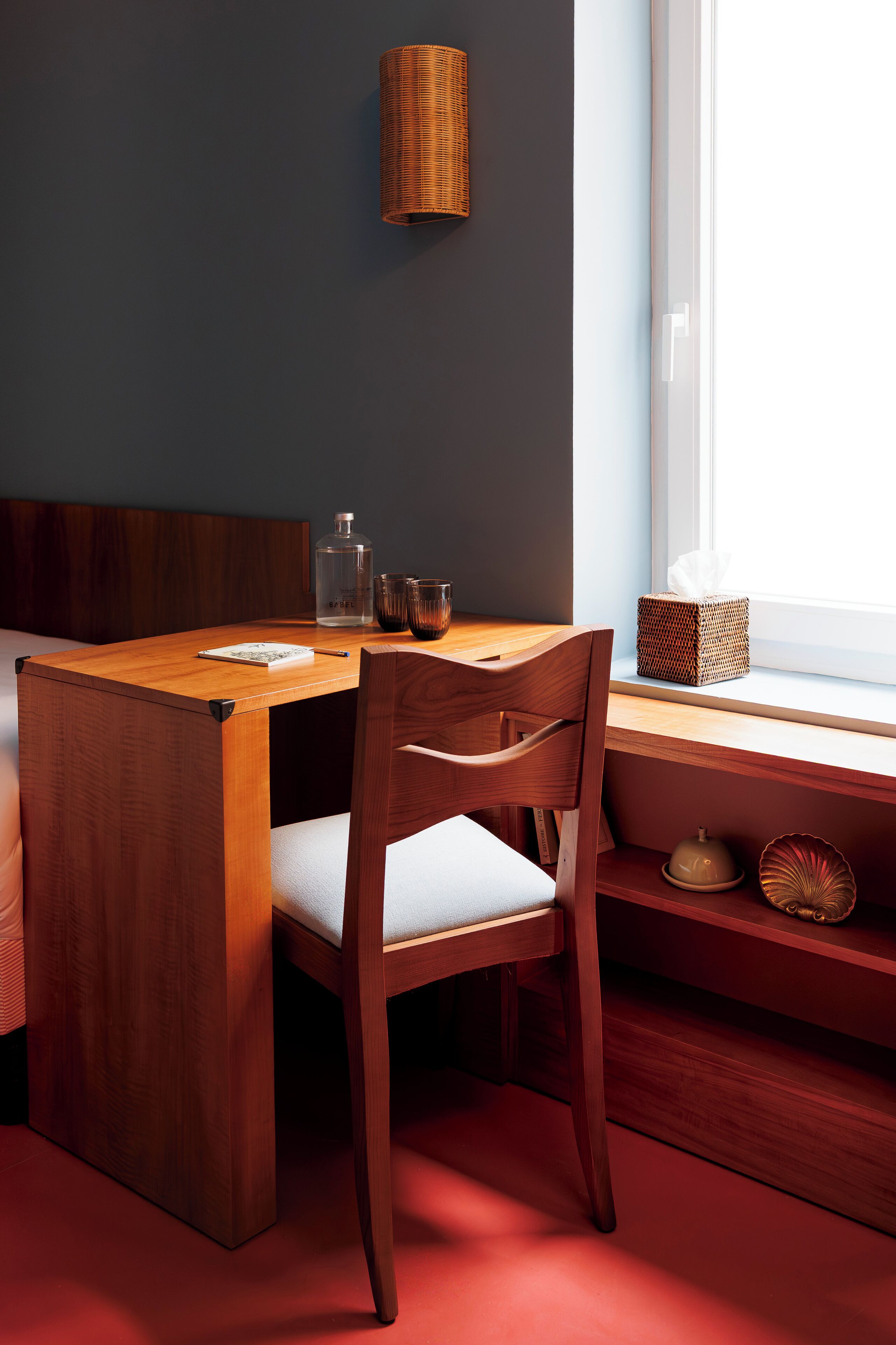 Una mesa de comedor de madera con una silla, una lámpara de mimbre y una ventana con vistas.