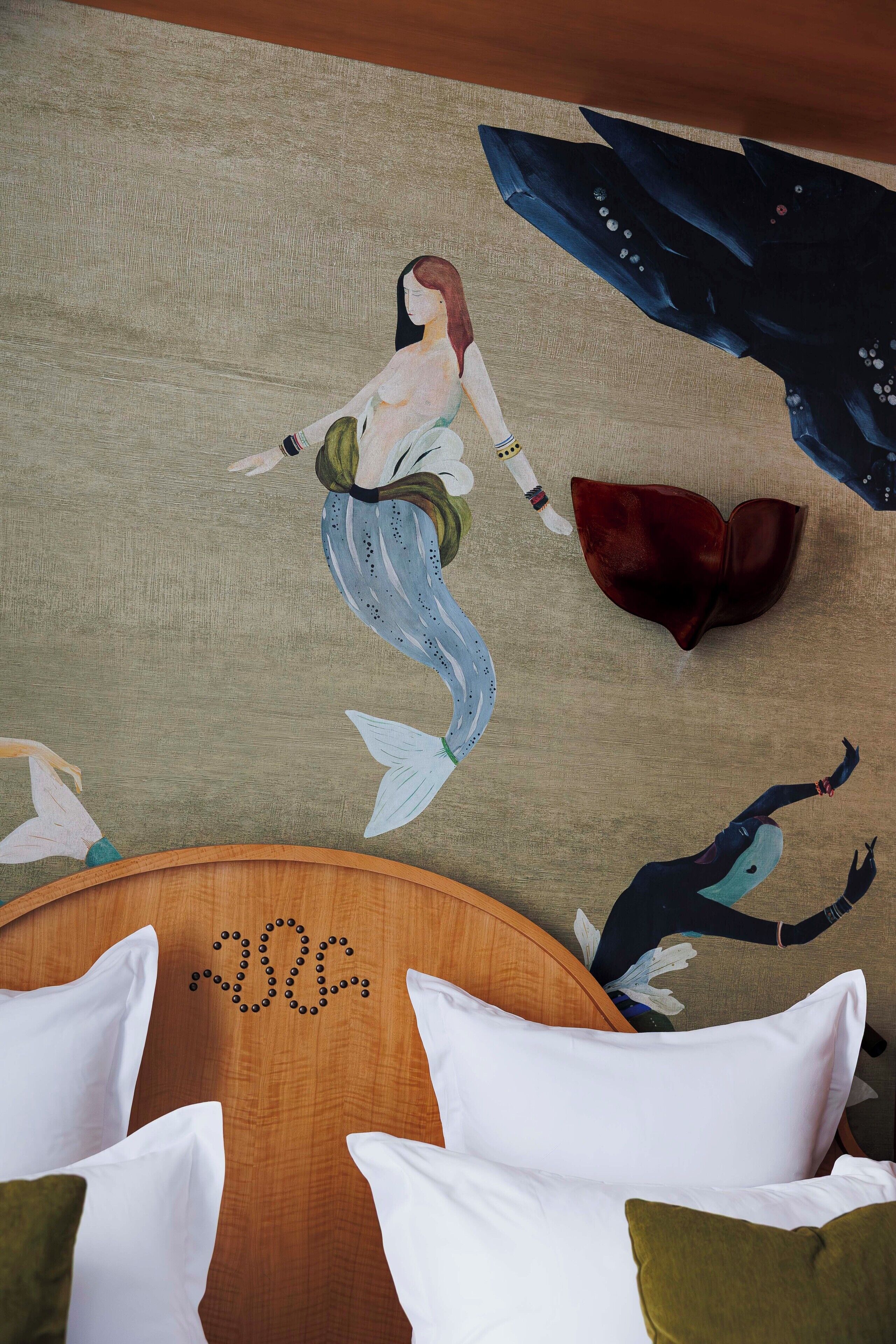 A room with a wooden headboard, white pillows, and a mural of a mermaid.