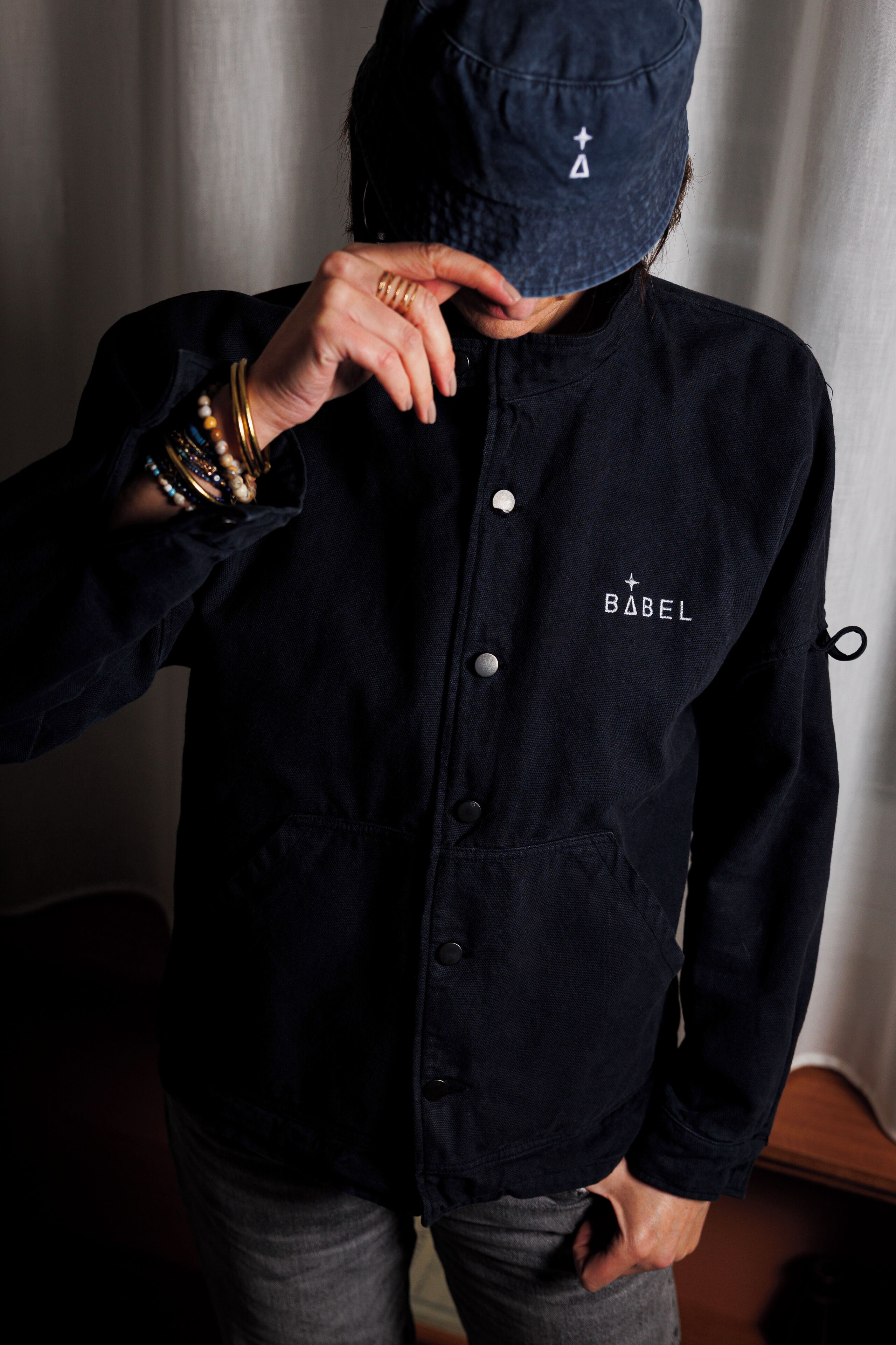 A person wearing a dark blue jacket with a hood and the word "BABEL" on the chest.